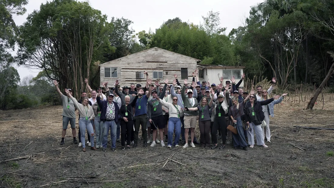 The full bus tour group gathered in front of an original house on a development site